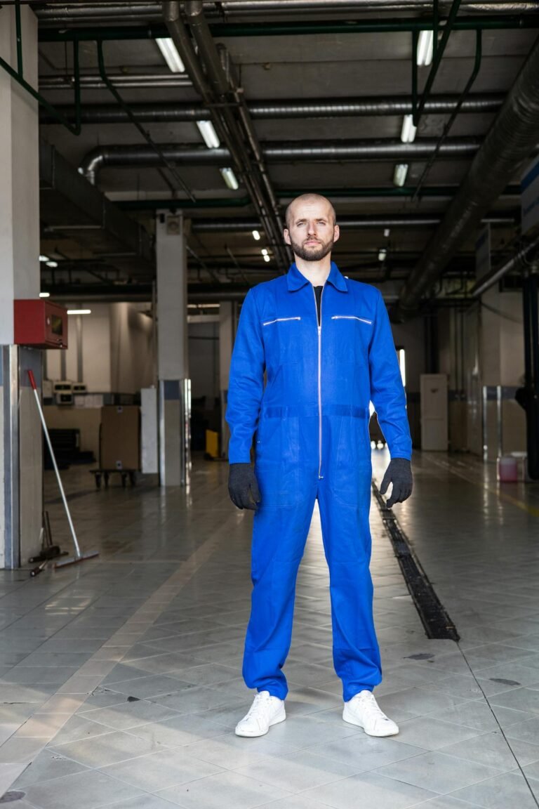 Mechanic in blue coverall standing confidently in an auto repair shop.